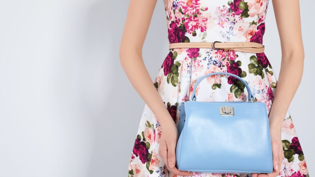 Woman wearing a floral print wedding guest dress for summer holding a blue handbag.